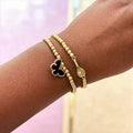Gold beaded bracelet with a black clover charm.